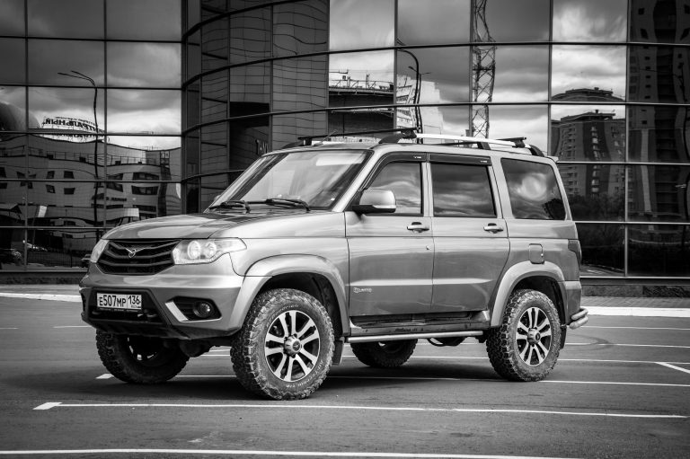 Black and white photo of SUV against modern reflective glass building in city.