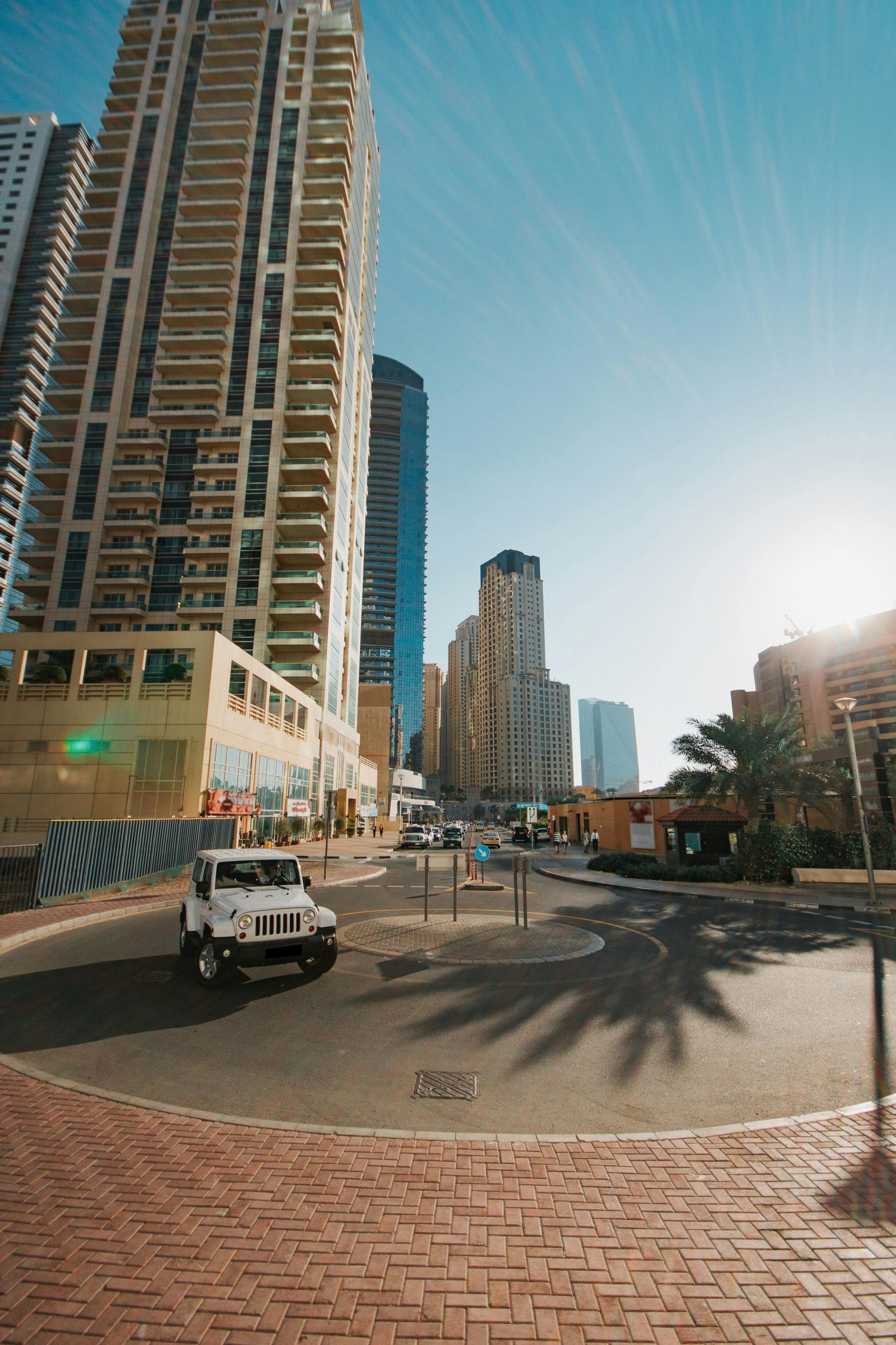pexels-photo-5075091-5075091 Street view of a modern city with skyscrapers under bright sunlight and a vehicle on the road.